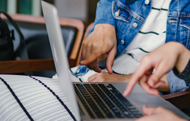 Two people sat down at a laptop pointing at screen