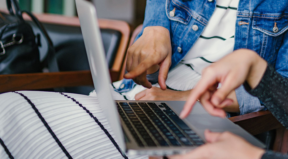 Two people sat down at a laptop pointing at screen