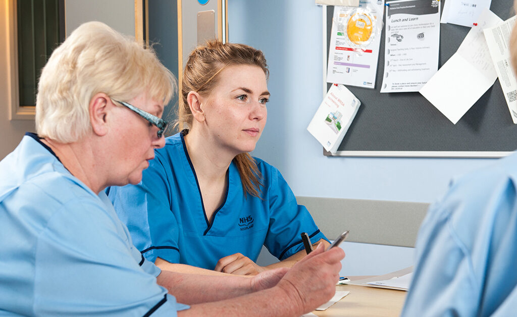 Nurses sat down at table with pen and paper in thought