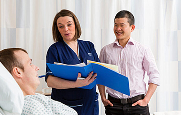Nurse holding folder talking to patient on bed