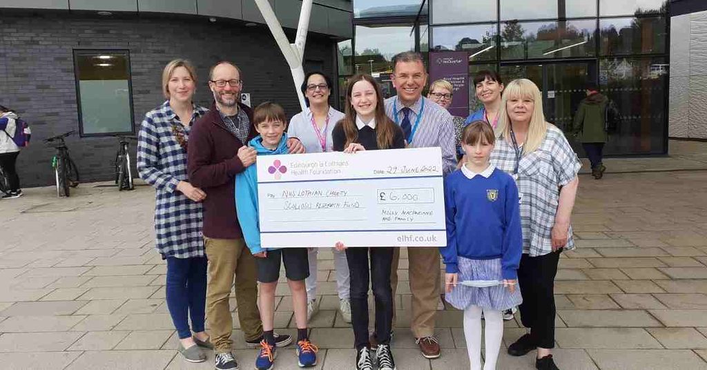 Teenages holding a large cheque for NHS Lothian charity