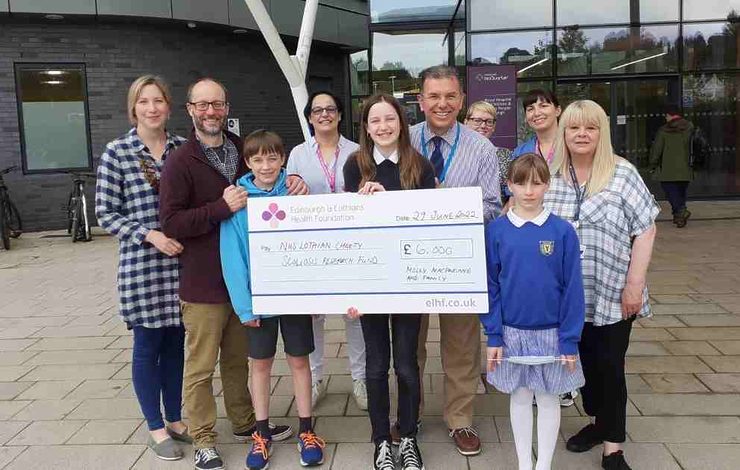 Teenages holding a large cheque for NHS Lothian charity