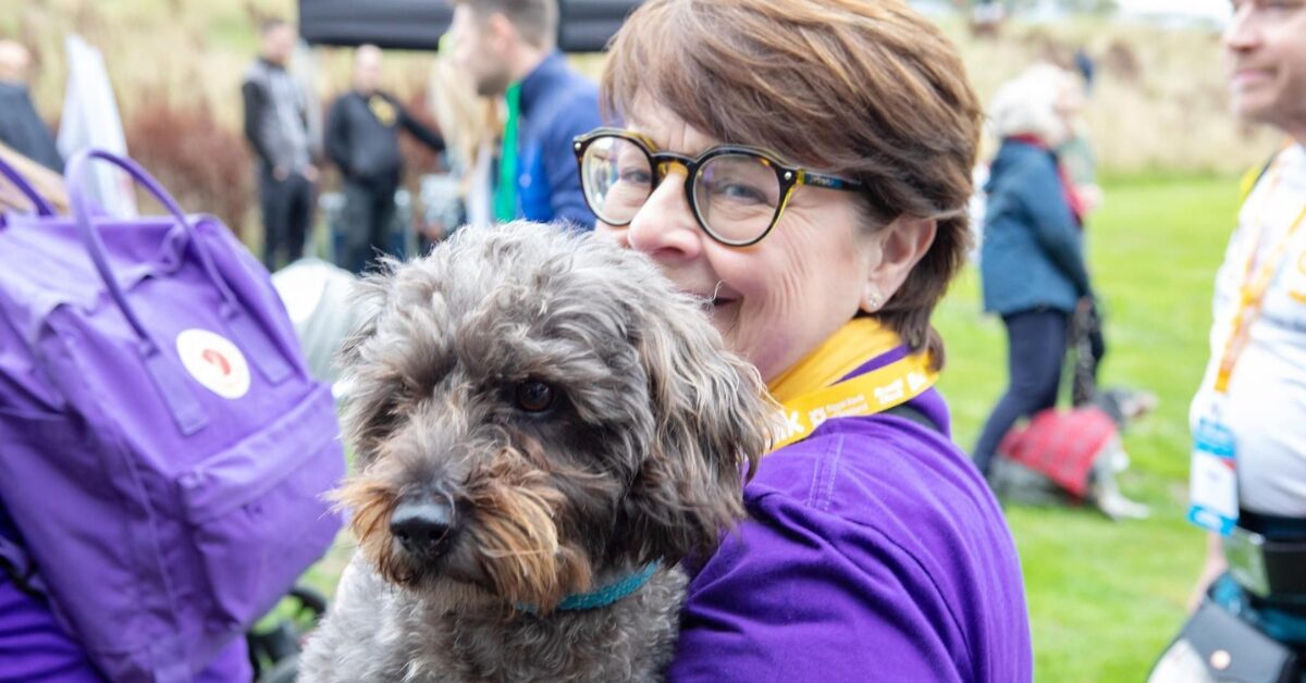 Elaine wearing an NHS Lothian Charity t-shirt smiling at the camera holding a dog