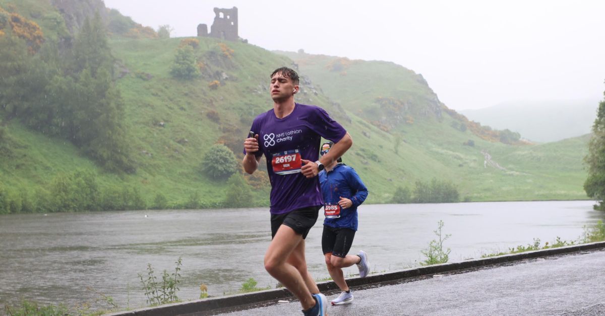 EMF runner, Ben, with his NHS Lothian Charity t-shirt on running on the road past water