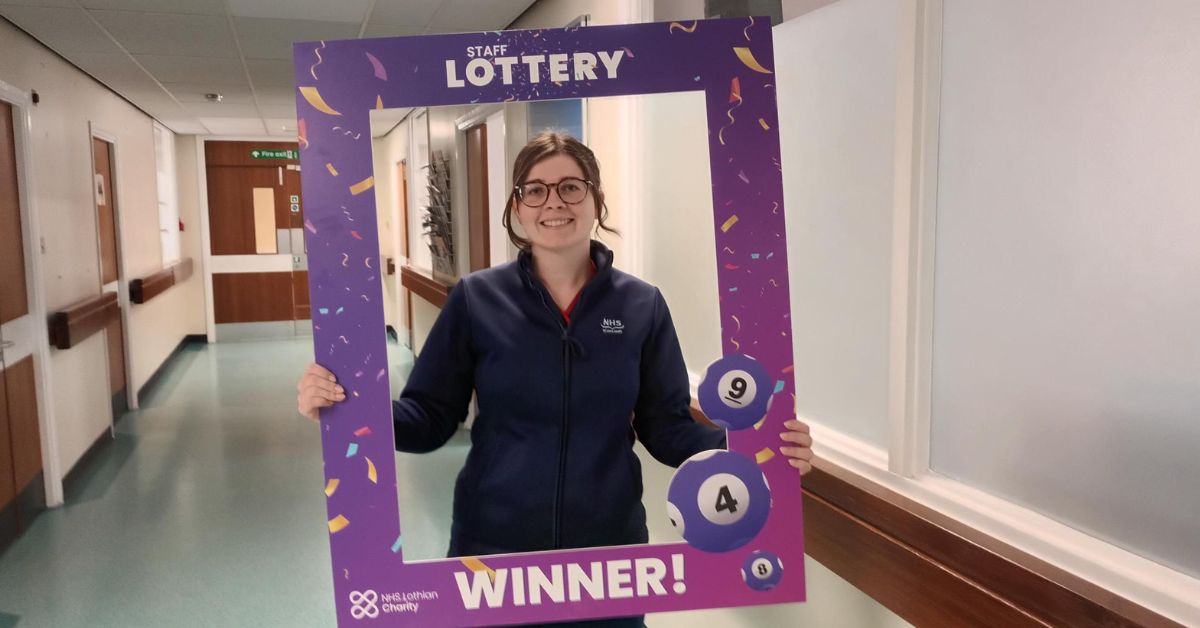 lottery winner, Erin, in a hospital corridor holding up the lottery winner frame