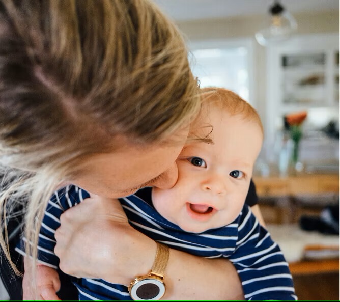 close up of a baby facing the camera being kissed by their mum