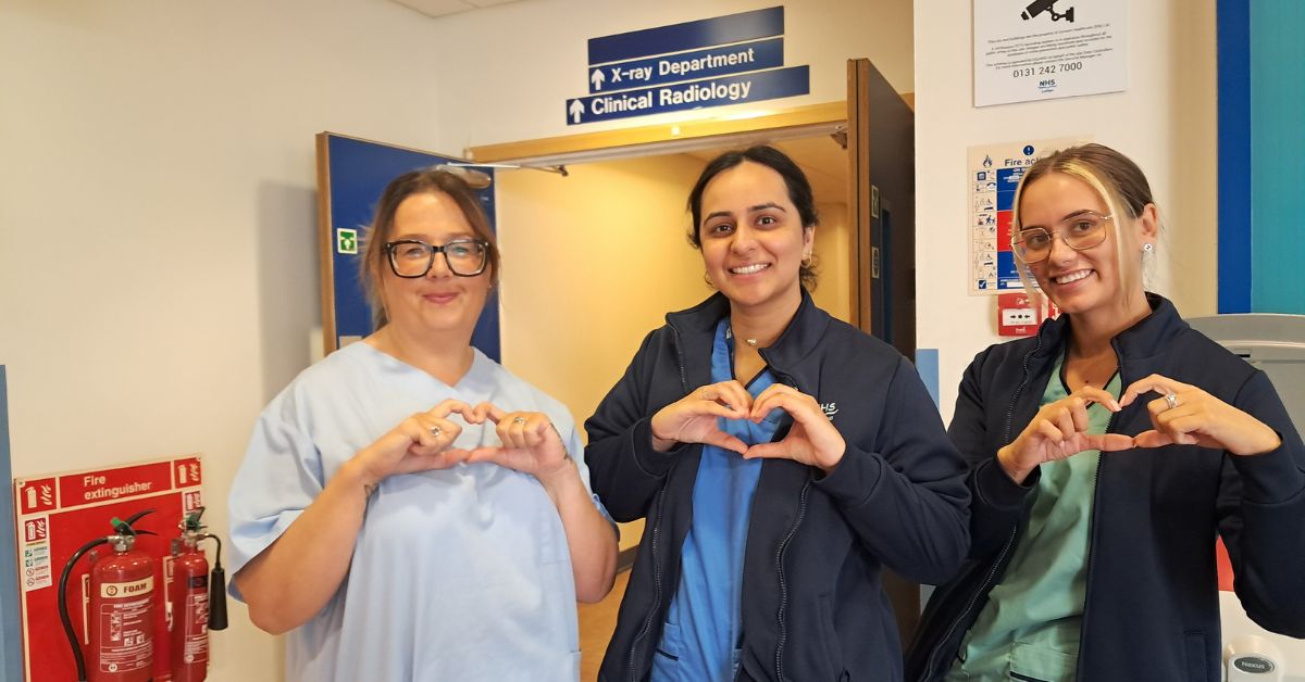 three members of staff in NHS uniforms facing the camera and making heart shapes with their hands