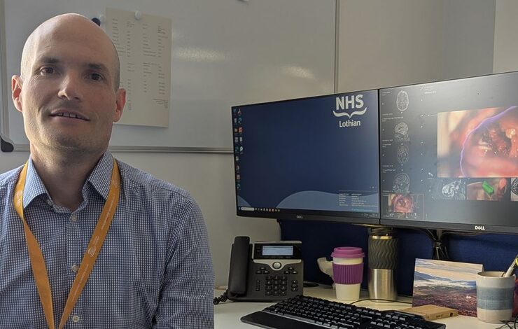 Mr Anthony Wiggans beside a computer showing the brainlab software